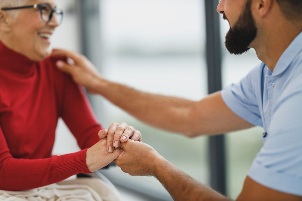 A caregiver rests a reassuring hand on a senior woman's shoulder